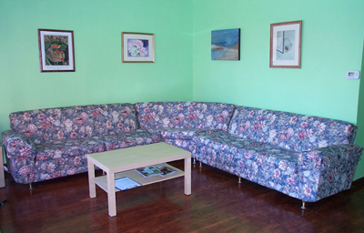 Reiki greeting, waiting and teaching room with soft green walls, decorative paintings, floral sofa, coffee table and dark wood floor.